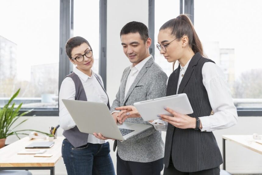 standing colleagues looking at laptop discussing about HR challenges and EOR solutions