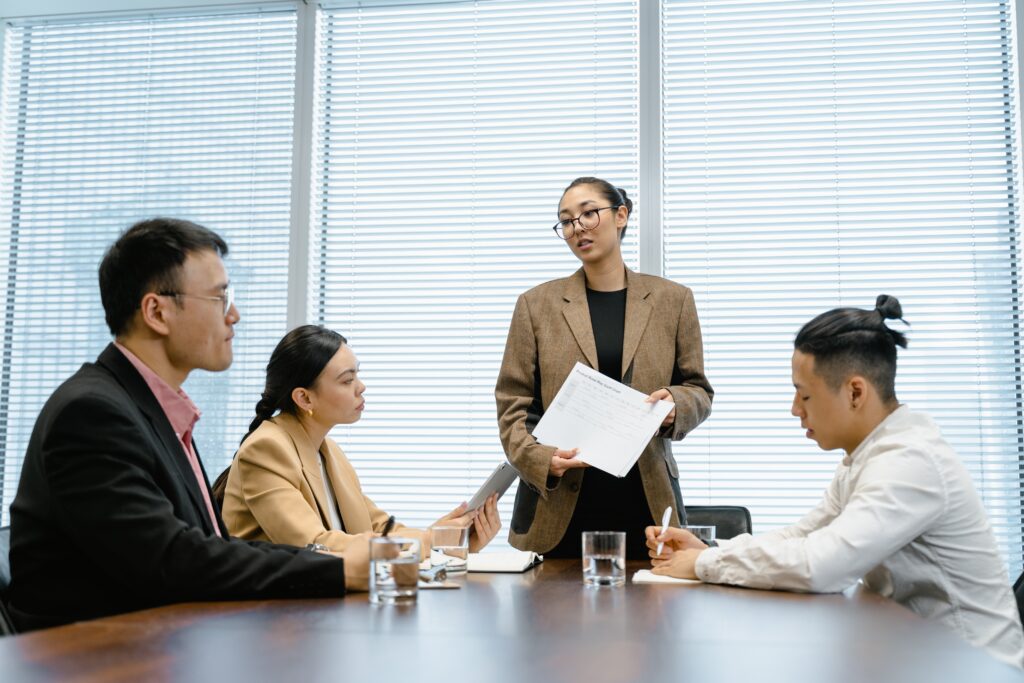 a woman holding a piece of paper in front of a group of people having a discussion about E-commerce interaction cost