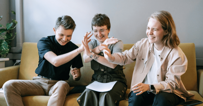 Three young people sitting on a couch with their hands raised, celebrating their recognition as the best workplace in IT-BPM.
